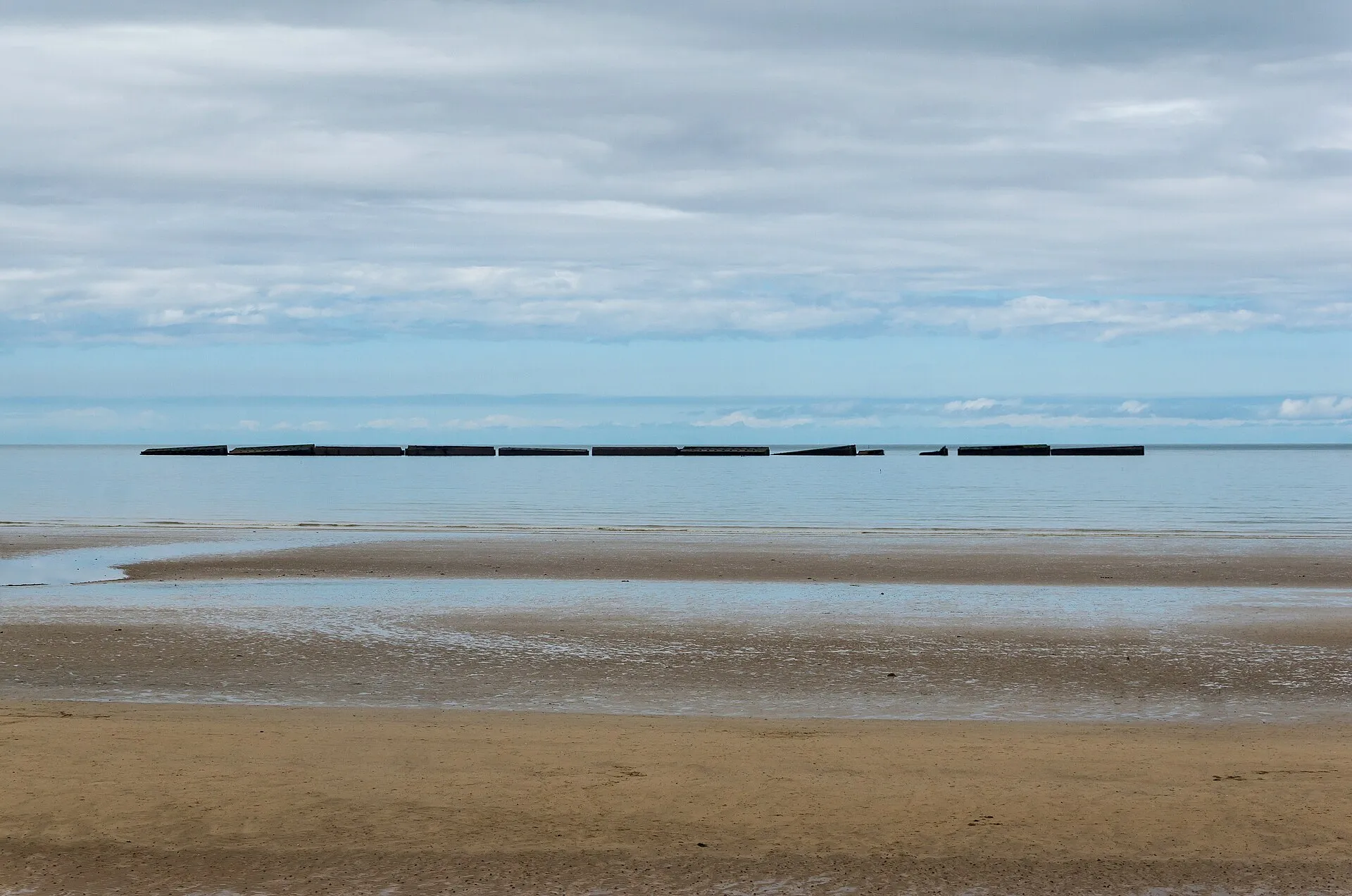 Les caissons du port artificiel Mulberry alignés sur l’horizon, vus de la plage d’Arromanches